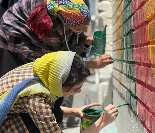 چند تا از داوطلبهای تیم بازسازی در حال رنگ زدن دیوار بیرونی مدرسه ابتدایی دخترانه چمران در منطقهٔ راه آهن تهران